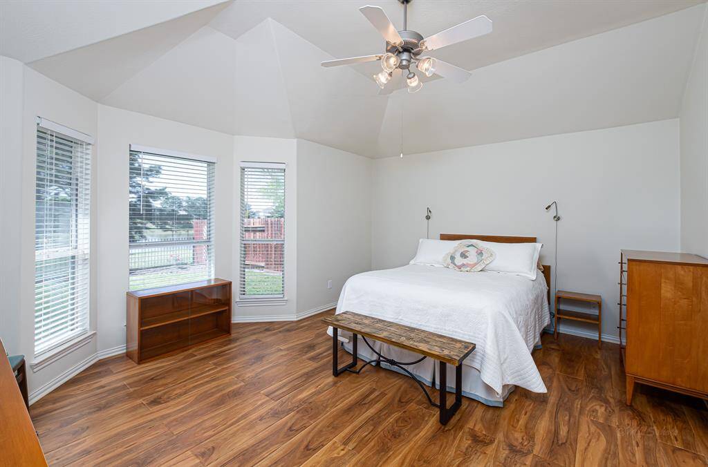 The spacious primary bedroom features beautiful flooring and unique ceiling architecture, complemented by windows that offer serene green space and pond views.