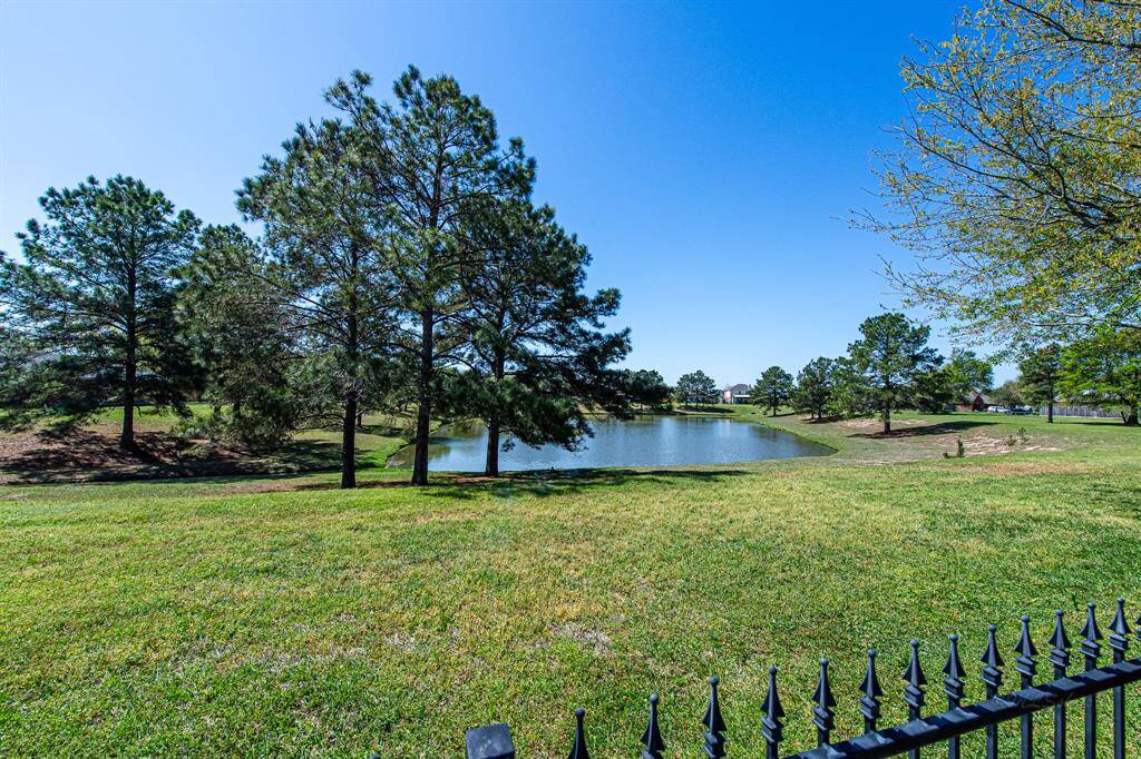 The lush green backyard slopes down to a picturesque neighborhood pond, a frequent gathering spot for local birds. The wrought iron fence creates an open feel, seamlessly blending the backyard with the surrounding landscape, while beautiful mature trees frame the pond, enhancing the scenic view.