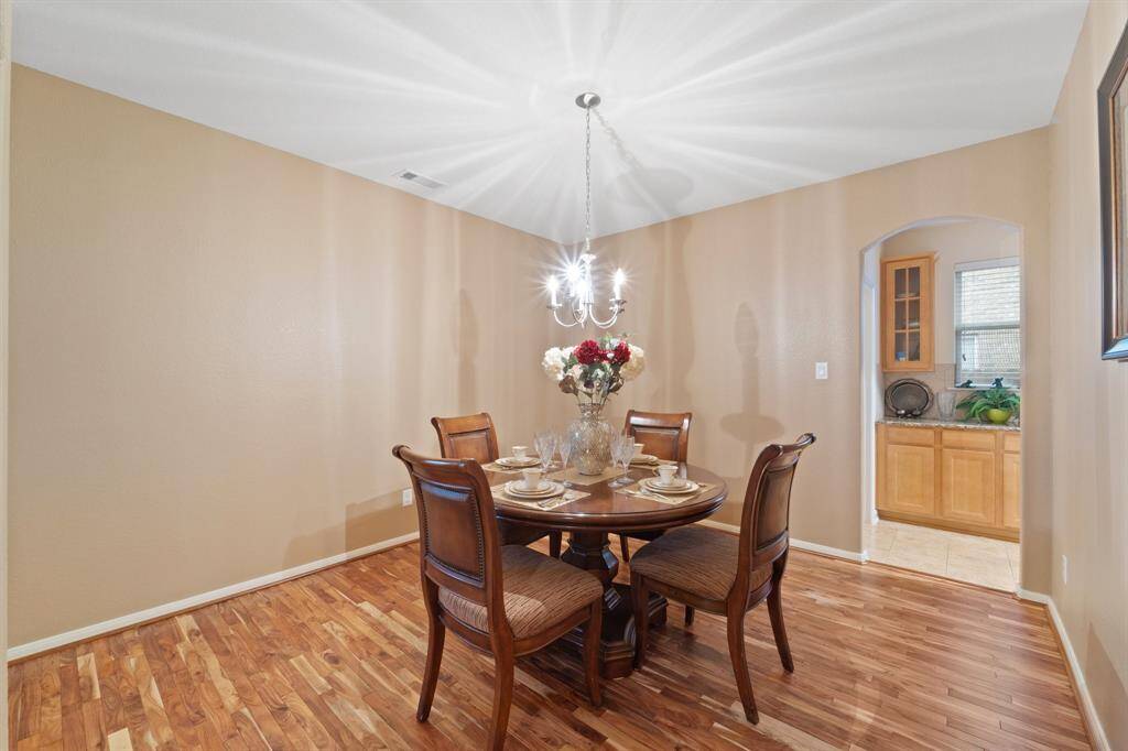 Elegant formal dining room features a modern chandelier, wood floors, and direct access to the kitchen through an arched doorway.