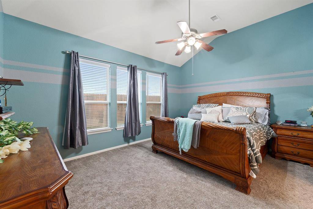 Spacious primary bedroom with soft carpeting, vaulted ceilings, and a wall of windows that allow natural light to fill the space.