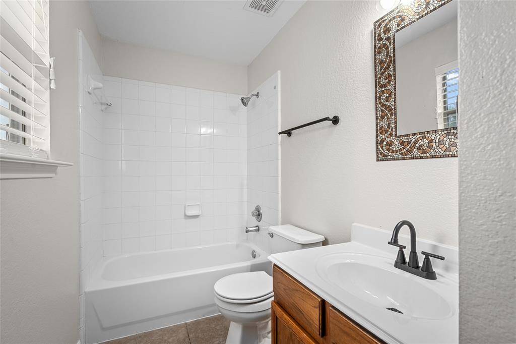 Your secondary bathroom has a clean, modern design with a white tile shower and tub, a stylish vanity with dark fixtures, and a decorative mirror. Natural light enters through the window creating a bright and attractive space.