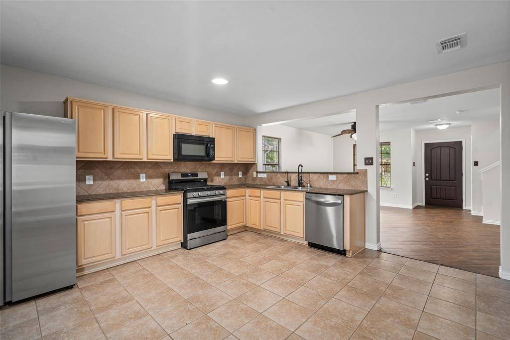 Your spacious kitchen includes light wood cabinets, stainless steel appliances, and tiled flooring. The open layout connects to a bright living area with tile floors and a welcoming entryway.