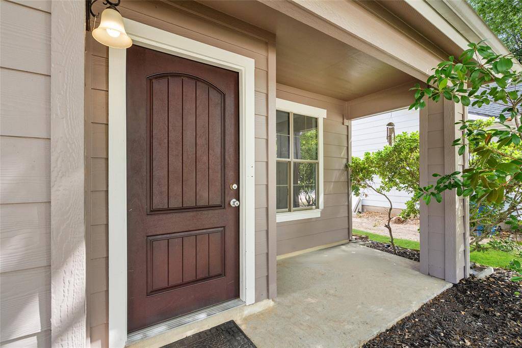Your new home has a lovely front porch with a wood-paneled door, warm outdoor lighting, and a small garden area with greenery creating a cozy entrance.