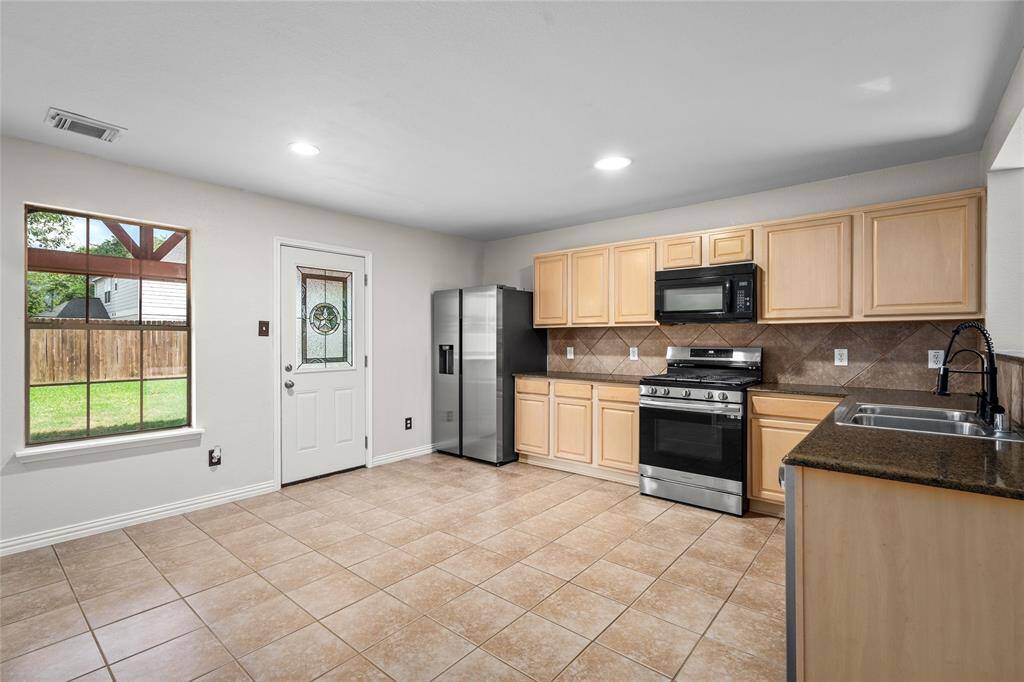 Your kitchen features tile flooring, light wood cabinets, and modern stainless steel appliances including a refrigerator and gas range. A window and glass-paneled door provide natural light and access to the backyard.