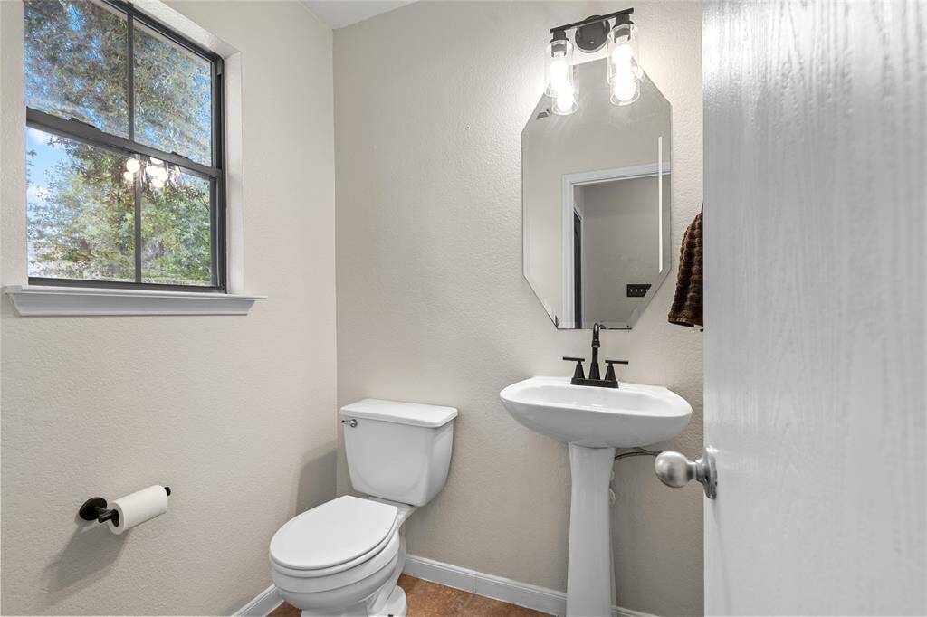 Your downstairs half bath has a pedestal sink with a modern mirror and light fixture above it. A window provides natural light. The room has light-colored walls and a simple, clean design.