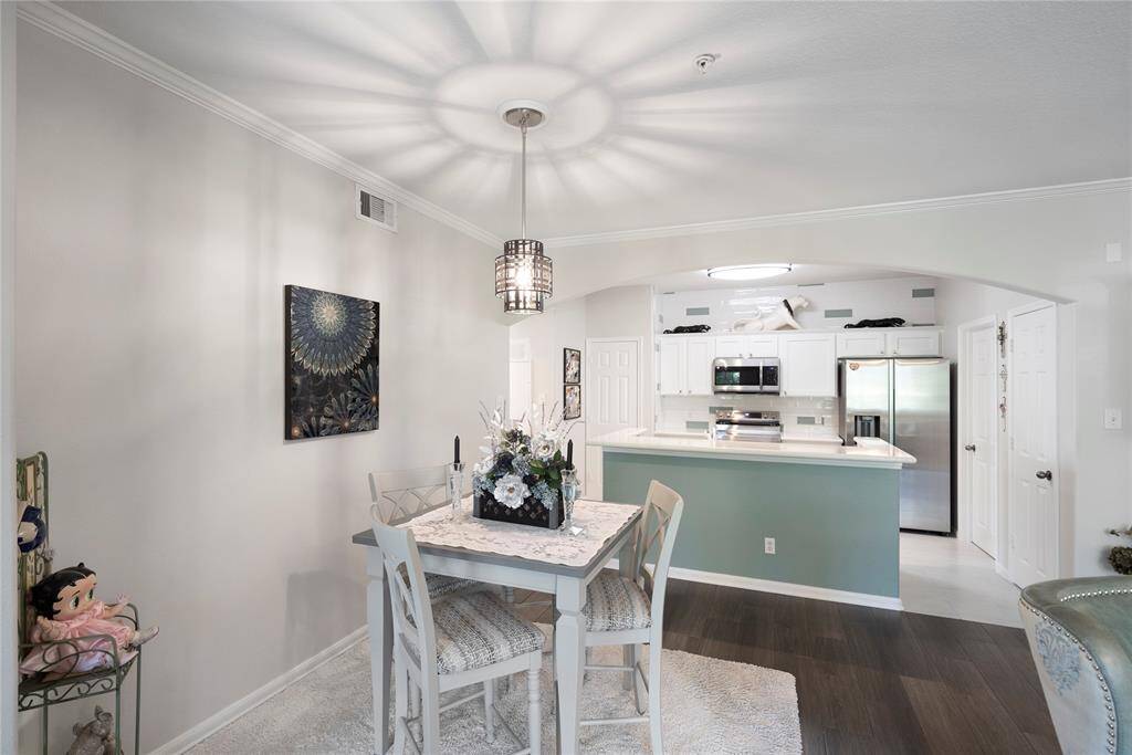 This is a bright, open-concept dining area that flows seamlessly into the kitchen, featuring modern lighting fixtures, a neutral color palette, and wood flooring, creating a welcoming space for entertaining and dining.