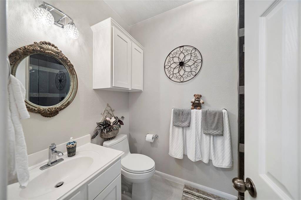 This is a neatly presented, modern bathroom featuring a white vanity with a classic framed mirror, and a wall-mounted cabinet for storage. The bathroom is well-lit with a stylish light fixture above the mirror.