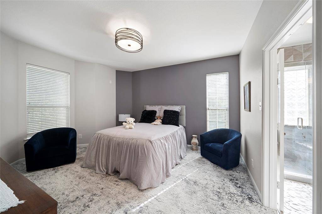 Modern bedroom featuring a neutral color palette with a contrasting accent wall, two large windows for ample natural light, and direct access to an en-suite bathroom.
