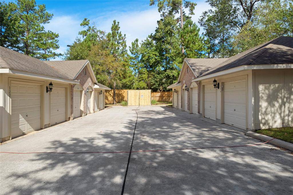 This photo shows a row of attached individual garages with ample driveway space, set against a backdrop of mature trees.