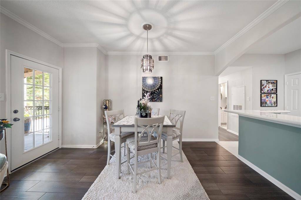 This is a bright and modern dining area featuring a stylish table set for four, elegant dark flooring, and access to an outdoor balcony through sliding glass doors. The room is well-lit with a contemporary light fixture and has a neutral color palette that creates a welcoming atmosphere. The island separates the space from an adjacent area, maintaining an open feel.