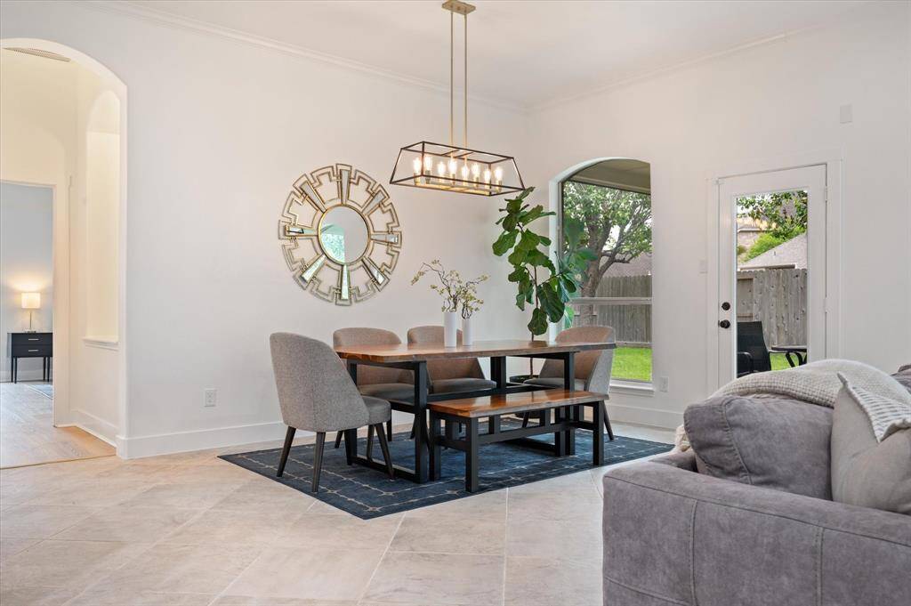 The dining area is beautifully accented by an elegant lighting fixture above the table, drawing the eye upward. A large picture window floods the space with natural light, offering stunning views of the backyard. This area also provides seamless access to the expansive outdoor living space, enhancing the home’s effortless indoor-outdoor flow.