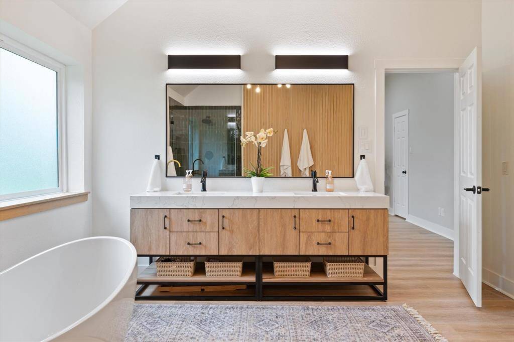 The stunning vanity features a thick marbled countertop, dual sinks, a stylish framed mirror, and updated lighting fixtures—combining elegance and functionality for your daily routine.