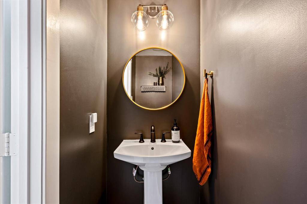 The powder bathroom exudes elegance, featuring a beautiful pedestal sink, a gold-framed mirror, and a sophisticated lighting fixture that perfectly complements the mirror. Moody decorator paint adds a touch of sophistication, enhancing the room’s stylish charm.