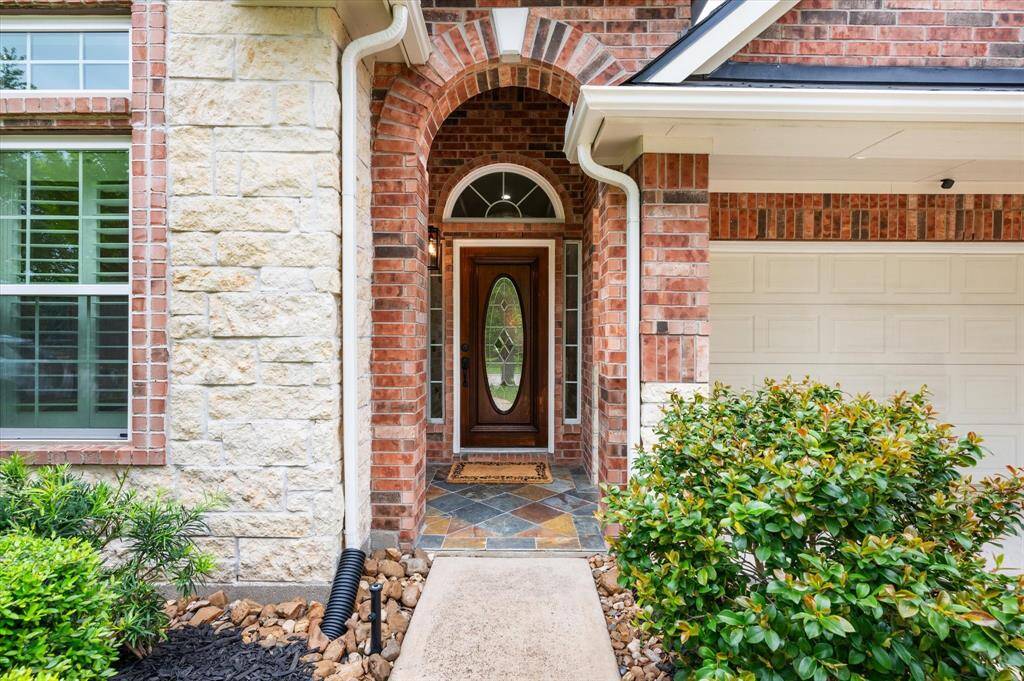 Follow the beautifully landscaped pathway to the inviting front porch, gracefully framed by a timeless brick archway. A leaded glass front door, complemented by transom windows, offers a warm and elegant welcome—hinting at the refined details that await inside.