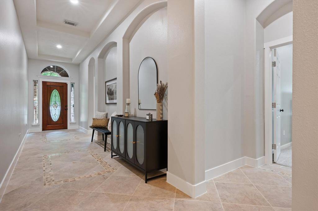 Welcome in! This elegant entryway immediately sets the tone with soaring tray ceilings and neutral tile flooring that exudes timeless sophistication. Thoughtful details such as decorative art niches, designer paint tones, substantial baseboards, and accent tile inlays add layers of refinement and visual interest throughout the space.