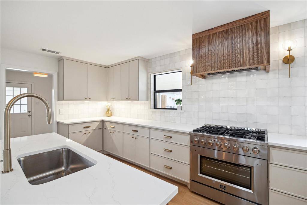 Sleek kitchen featuring a quartz countertop, 36’’ gas oven range, custom white oak vent hood with fluted wood, and custom-built cabinets with soft-close doors.