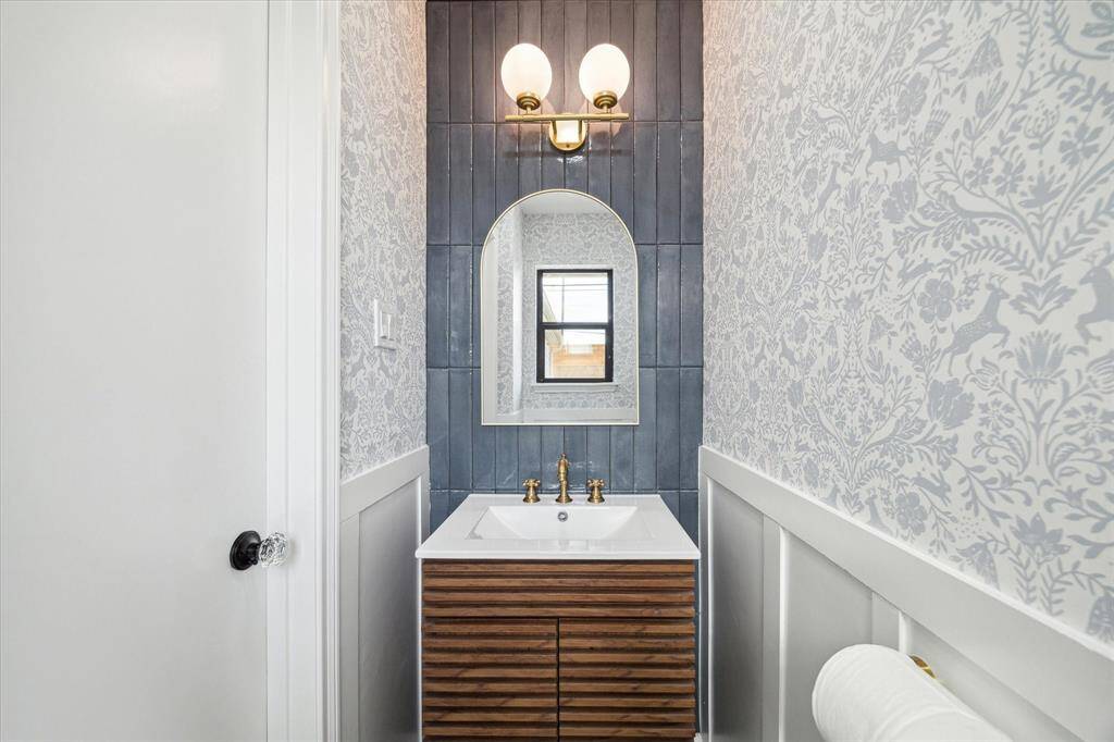 Elegant half bath with designer wallpaper and stunning gold lighting.