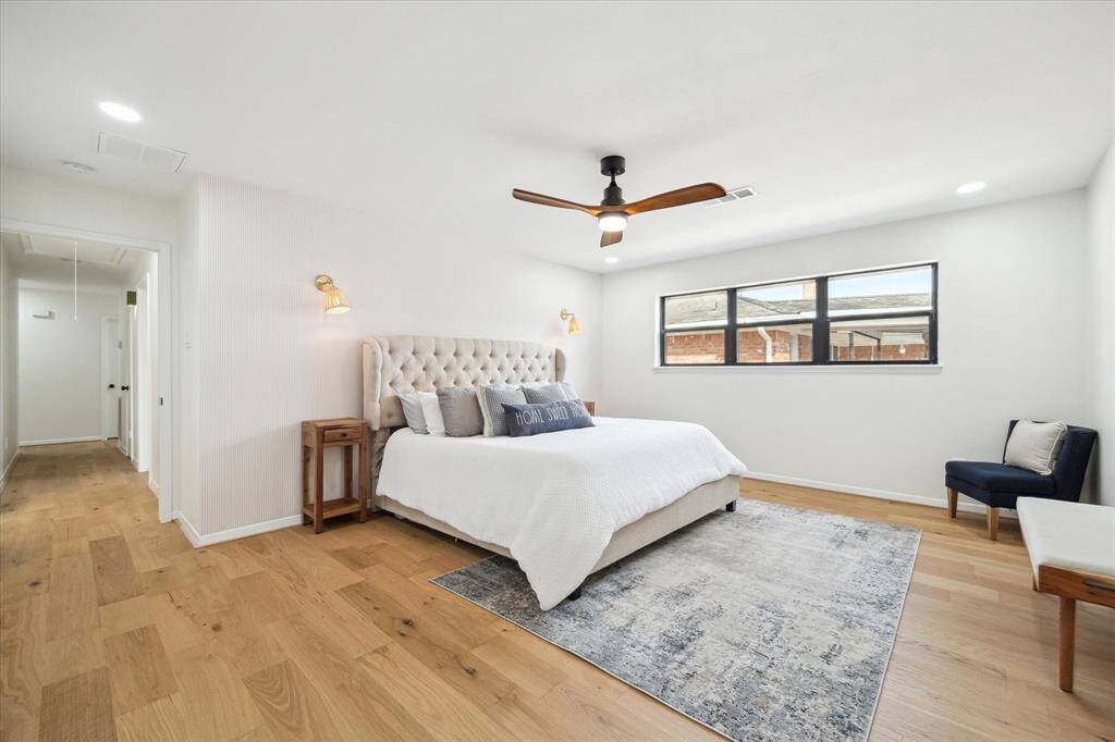 Serene primary bedroom with a ceiling fan, gold lighting, abundant natural light, and designer khaki and white wallpaper adds elegance.
