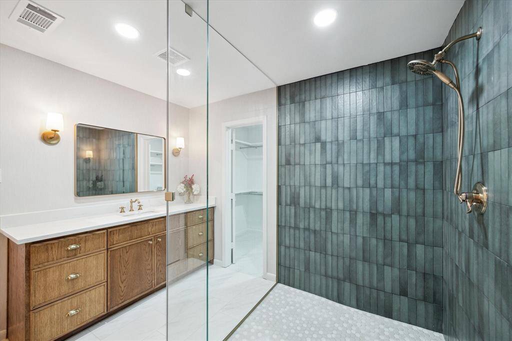 Sophisticated primary bathroom featuring Italian and Spanish porcelain tiles, a quartz countertop, designer gold lighting, and a glass-enclosed shower with Midori green tiles.