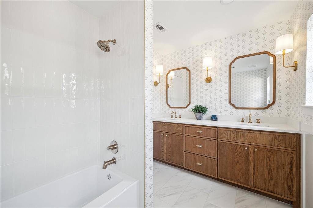 Stylish bathroom featuring designer wallpaper, Italian and Spanish porcelain tiles, a quartz countertop, designer gold lighting, and a tub and shower combo.