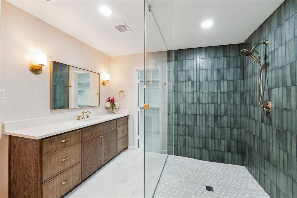 Sophisticated primary bathroomfeaturing Italian and Spanishporcelain tiles, a quartzcountertop, designer gold lighting,and a glass-enclosed shower with a beautiful Midori green wall tiles.