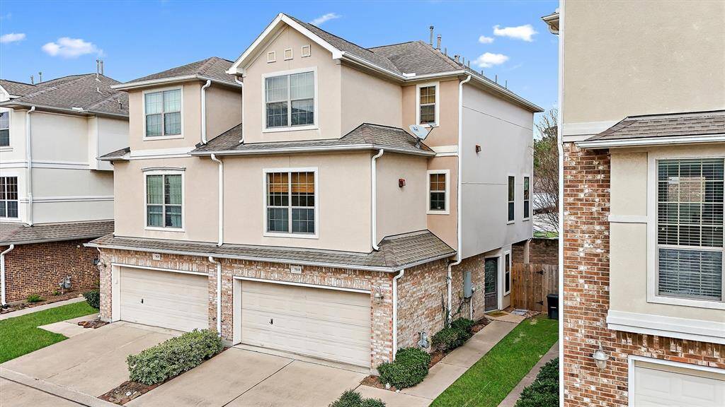 Modern three-story townhouse with a brick and stucco exterior. It features a two-car garage and a small fenced backyard. The property is located in a gated community with an appealing neighborhood feel.