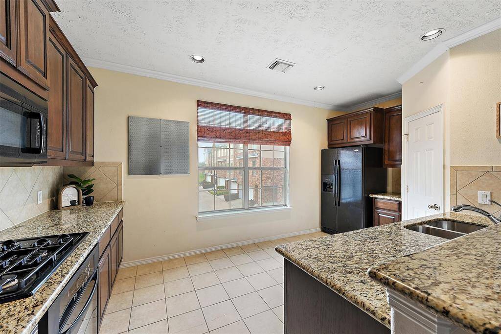 The kitchen features granite countertops, dark wood cabinetry, and a gas stove. It has a spacious layout with a large window providing natural light, tiled floors, and modern appliances.