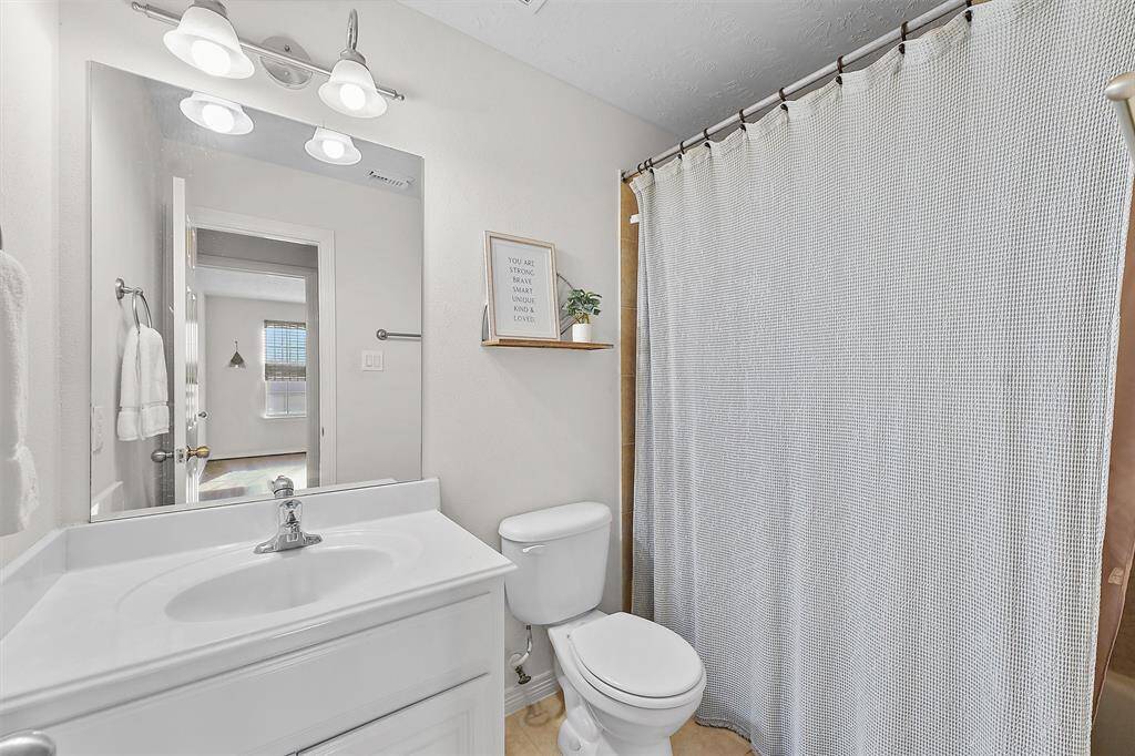 Second full bathroom is located directly across the hall from the secondary bedroom. It features a clean, modern design with a white vanity, large mirror, and a bathtub/shower combo.