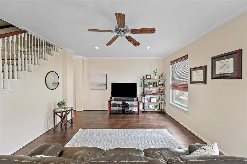 Bright living room with hardwood floors and neutral walls. Stairs with white railings add charm, while large windows provide natural light. Ideal for relaxation and entertainment.