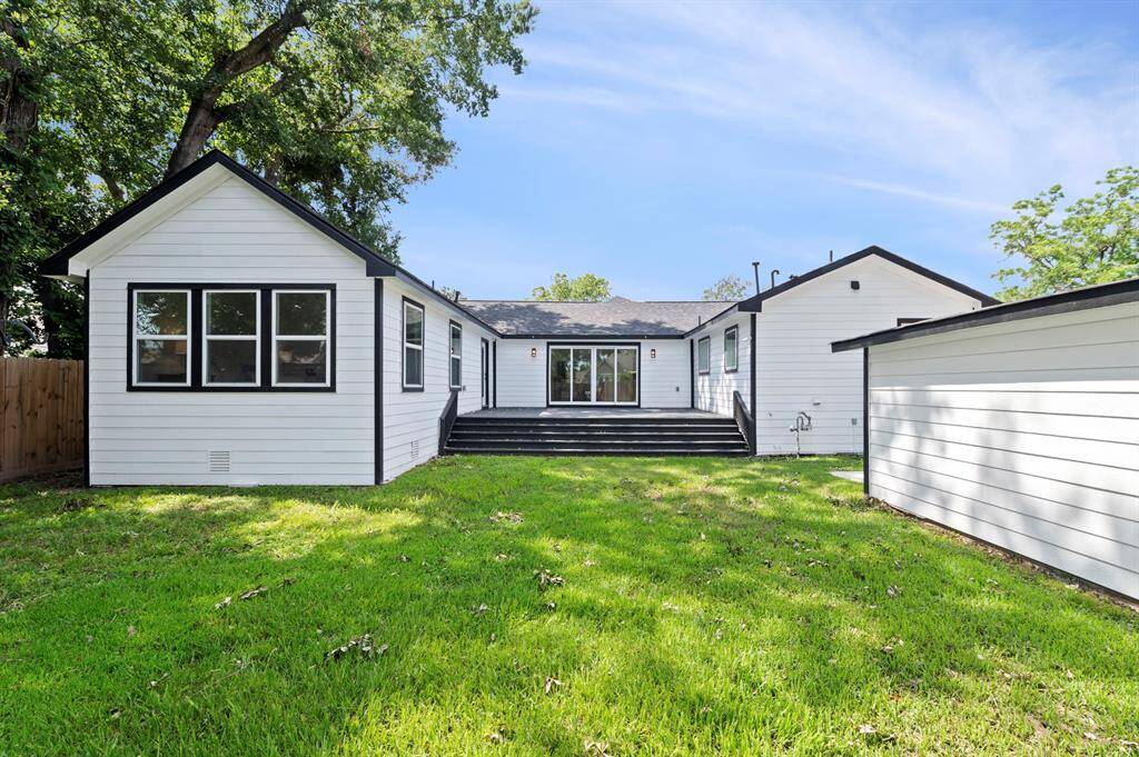This wide-angle shot shows off the full rear elevation—fresh siding, dual staircases, and a spacious deck perfect for entertaining under the trees.