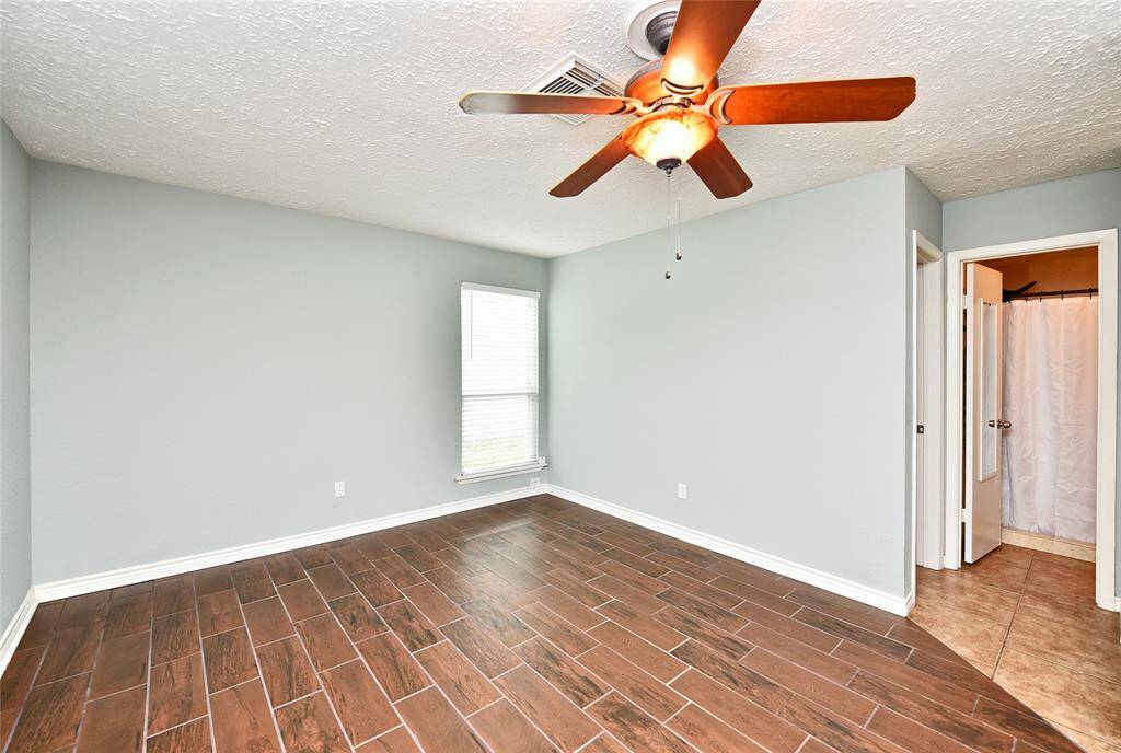 Lovely and tranquil primary bedroom also features wood look tile flooring throughout. The soft gray paint color adds to the tranquility. It doesn't look like it from this angle, but the room easily fits a king-sized bed with room to spare!