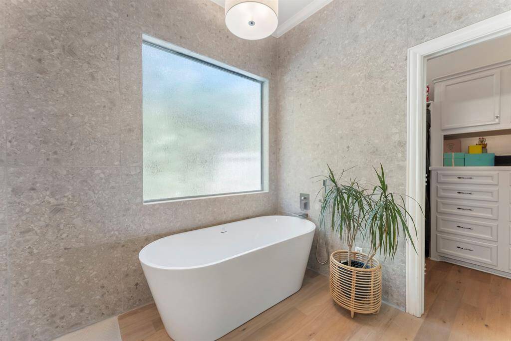 A large soaking tub invites relaxation, surrounded by floor-to-ceiling tile and complemented by a window that fills the space with natural light.