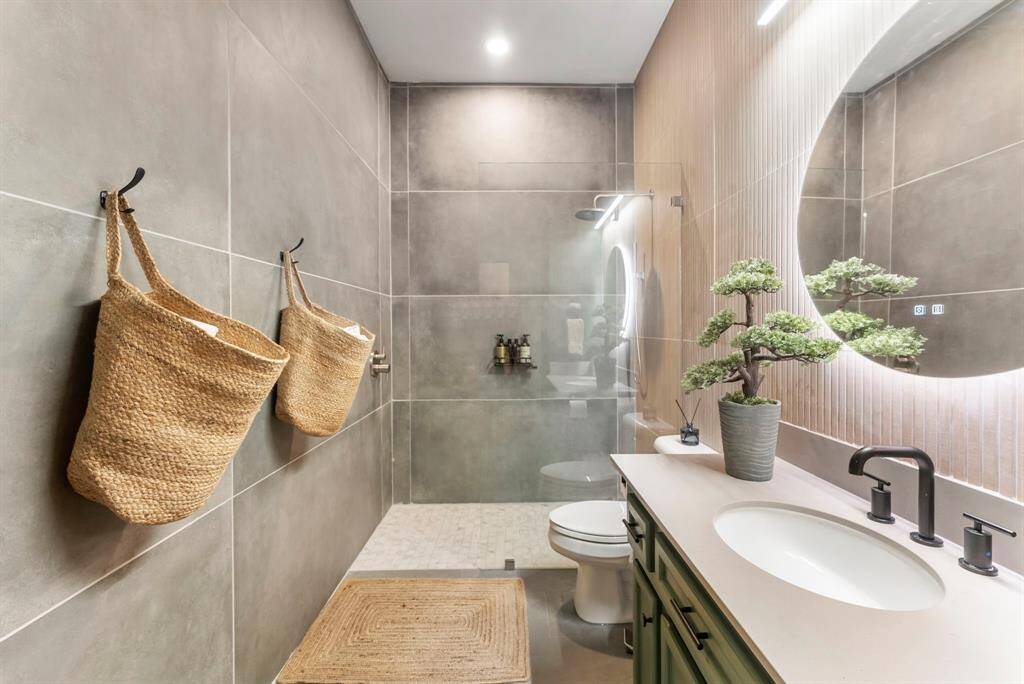 A gorgeous en-suite bathroom showcases floor-to-ceiling tile, a luxurious walk-in shower, and a stylish backlit mirror for a modern, spa-like experience.
