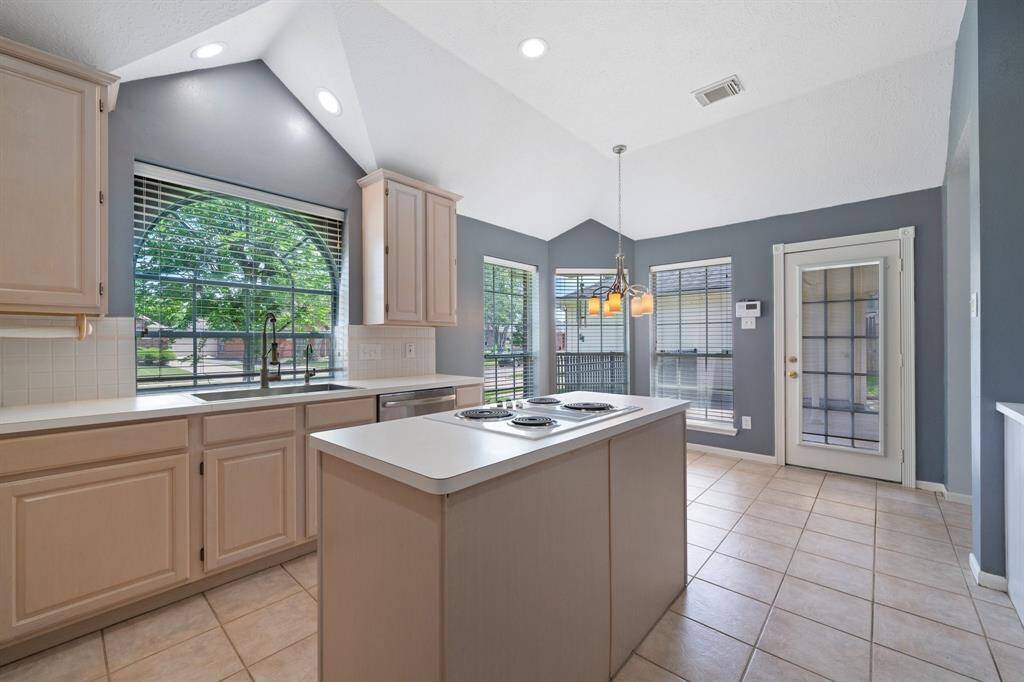 Beyond the dining room and laundry room is the spacious kitchen complete with an island with cooktop, high ceilings, large window at the sink, and it open to the breakfast and family rooms.
