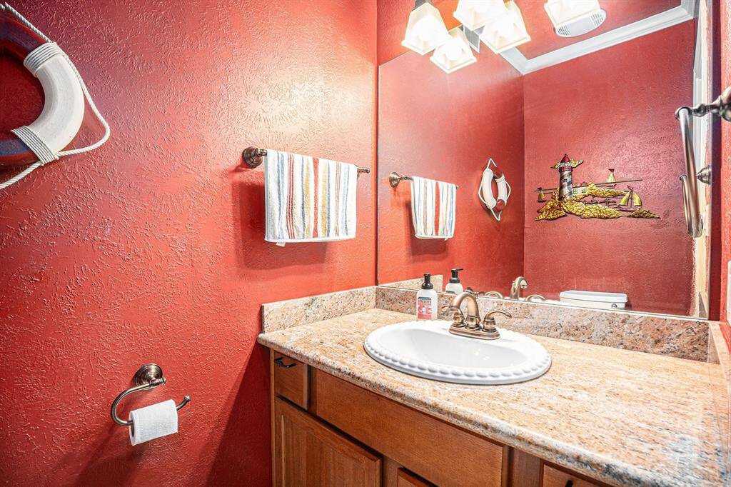 Conveniently located off of the living room, the half-bath features a stylish vanity with a granite countertop and a decorative mirror. The walls are painted in a vibrant color, complemented by nautical-themed accents.