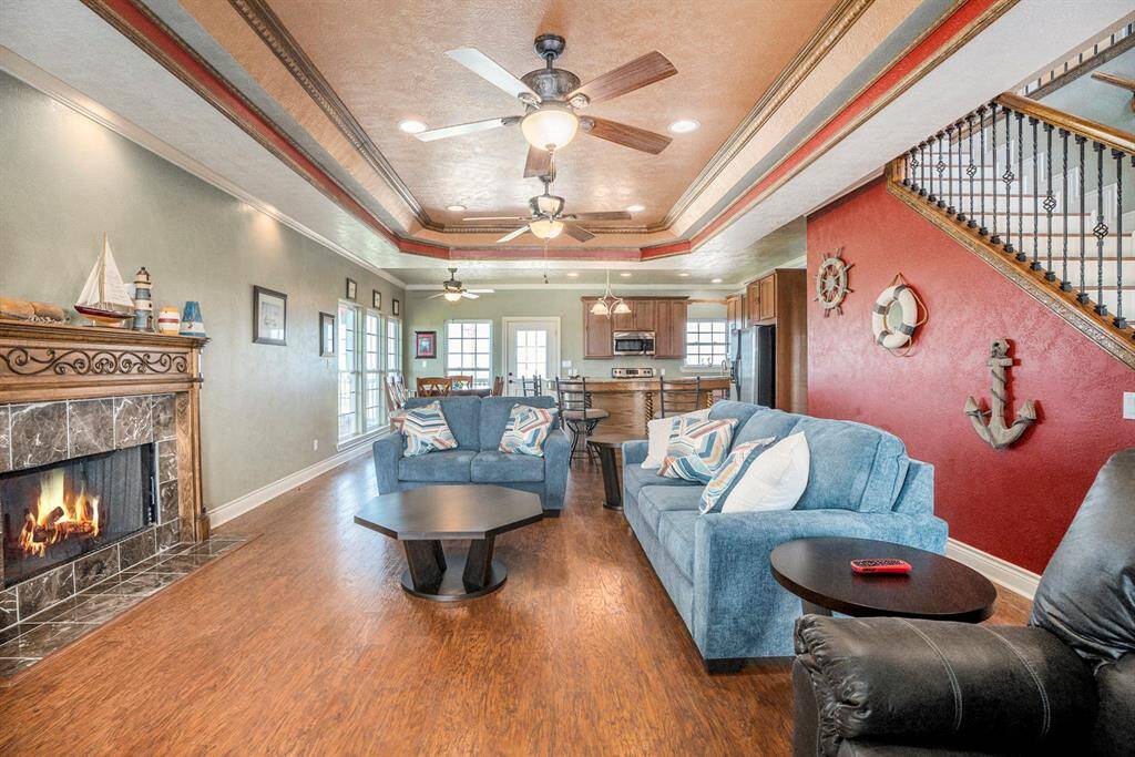 Inviting, open living room with hardwood floors and stone fireplace, flowing to kitchen/dining. Features a vibrant red accent wall with nautical décor. Abundant natural light fills the space through well-positioned windows and a rear glass door, enhancing its bright and airy ambiance.