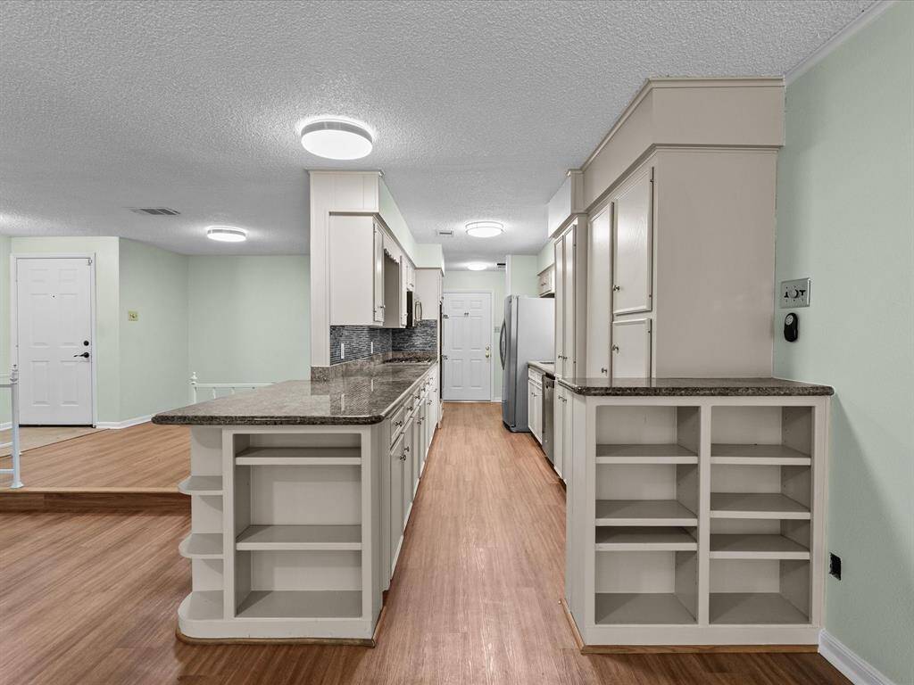 This photo showcases a spacious kitchen with light green walls and wood flooring. It features ample cabinetry, granite countertops, and modern appliances, providing a clean and functional cooking space.