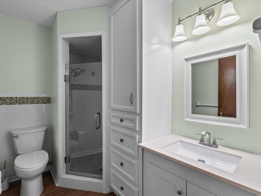 Primary bathroom features a large mirror with overhead lighting, and a white vanity with ample storage. It includes a toilet with safety bars and a shower area w/ grab bars, providing accessibility and convenience.