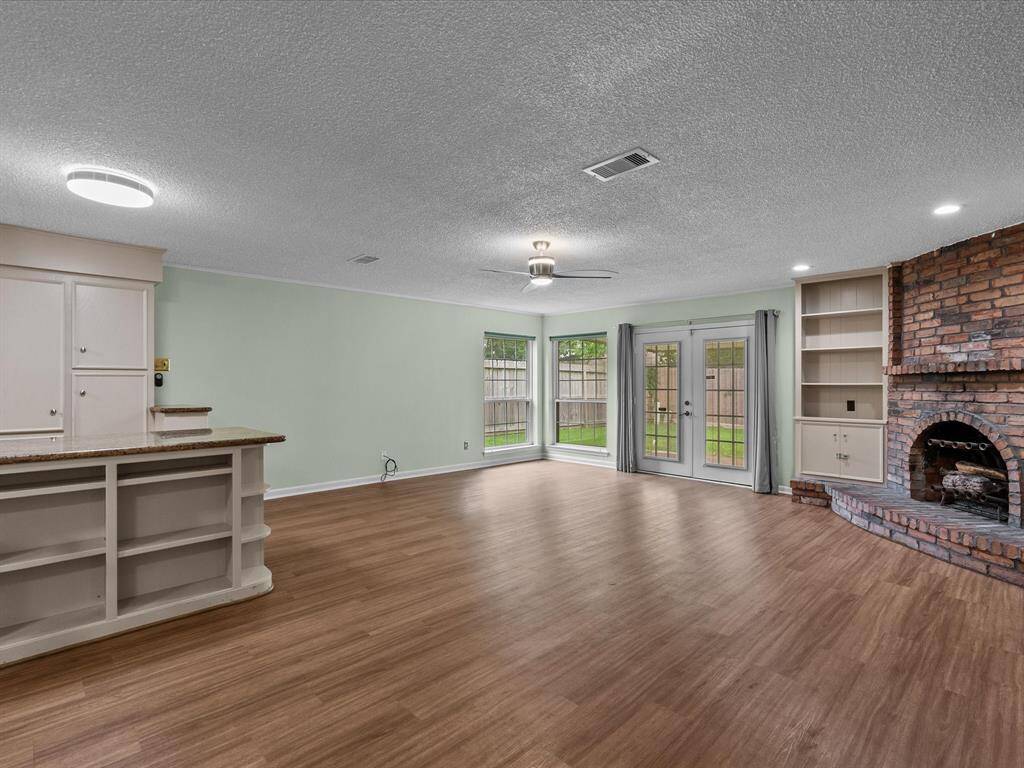 This spacious living area features tile wood flooring, a brick fireplace, and built-in shelves. It has lots of natural light from large windows and French doors opening to the backyard.