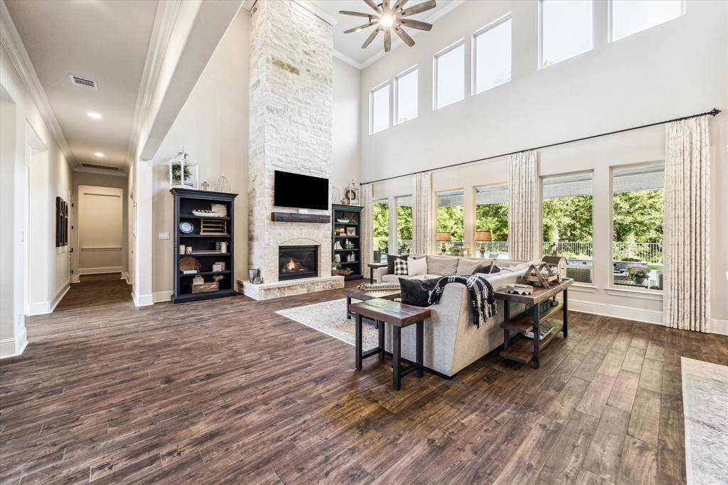 Anchored by a striking floor-to-ceiling stone gas-log fireplace, this impressive family room features a soaring 24' ceiling and a dramatic wall of stacked windows framing serene views of the pool, spa, covered patio, and lush wooded space behind the property.