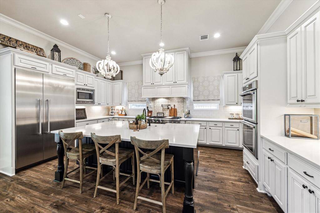 This chef-inspired kitchen is as functional as it is beautiful, showcasing Quartz countertops, custom cabinetry, designer tile backsplash, under-cabinet lighting, and elegant pendant lights over the island. High-end Thermador stainless steel appliances include double ovens and a gas cooktop with a pot filler. A spacious walk-in pantry and nearby utility room with added cabinetry provide exceptional storage and prep space, creating a layout that lives like a true butler’s kitchen.