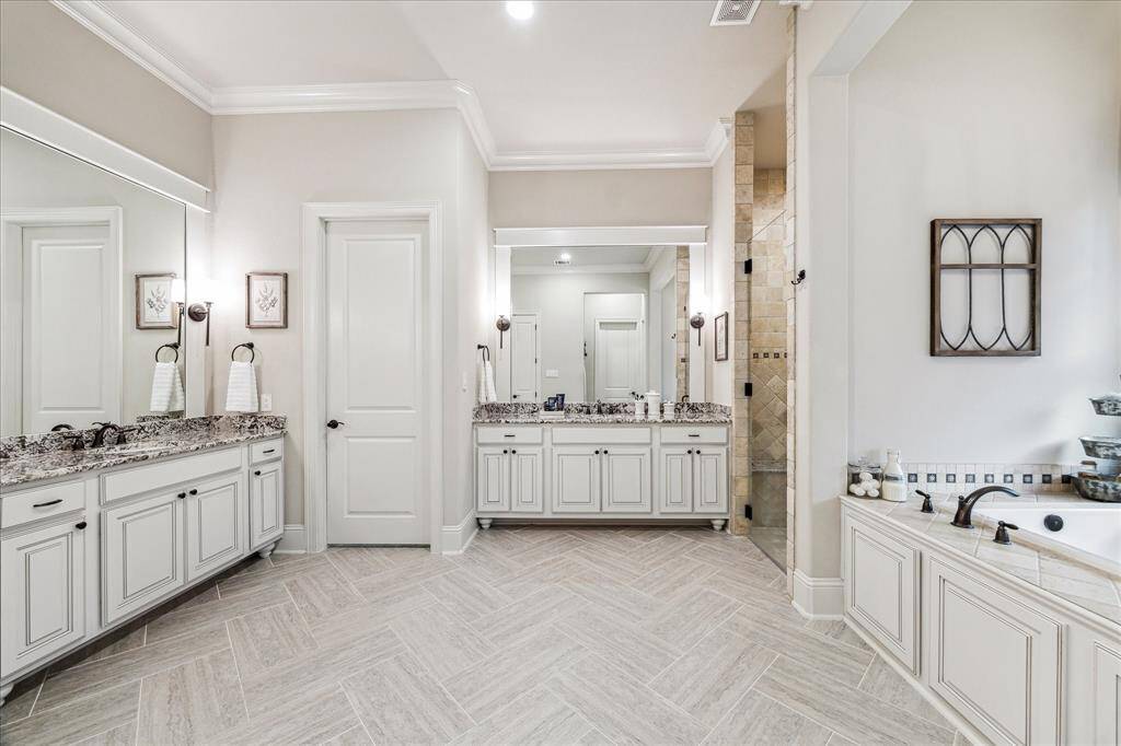This spa-inspired ensuite is a true sanctuary, featuring a deep jetted soaking tub, an oversized walk-in shower, and dual vanities with granite countertops, framed mirrors, and elegant lighting. Abundant cabinetry provides ample storage, while an adjoining bonus room offers a private extension of the retreat perfect for a home gym, yoga studio, or simply a quiet escape.