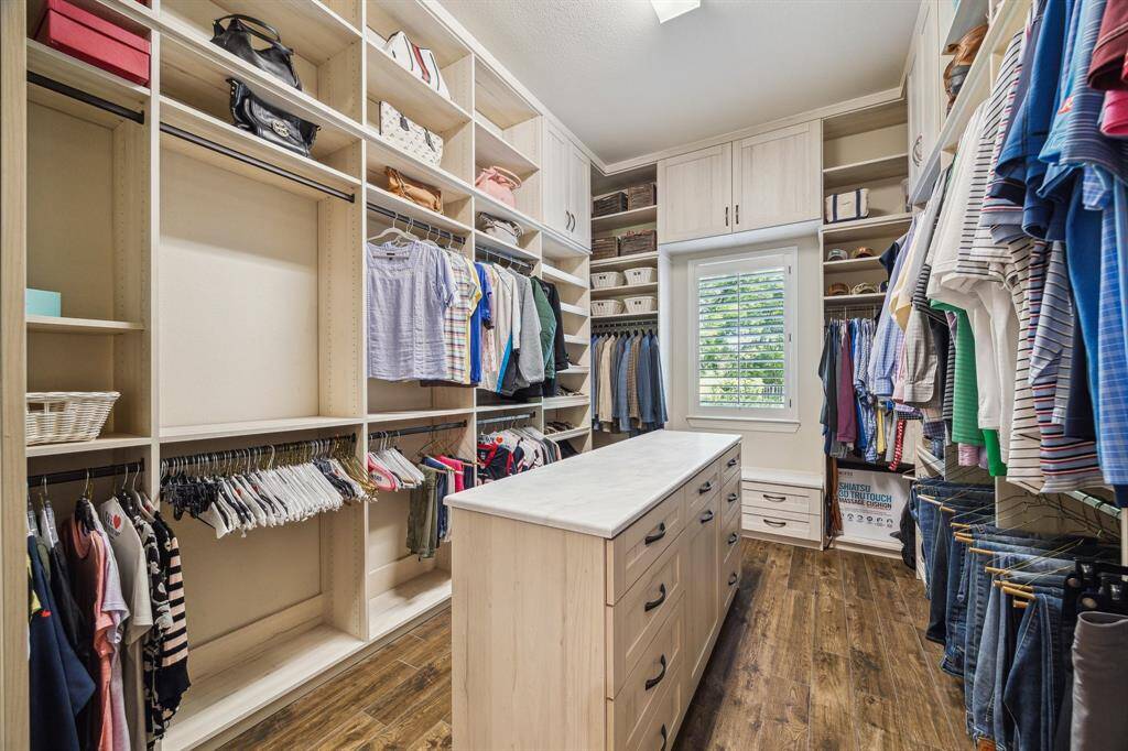 Another view of this fantastic, well equipped custom closet with wood-look tile flooring, large central island with additional storage, room for all your clothes, shoes, bags, and more.