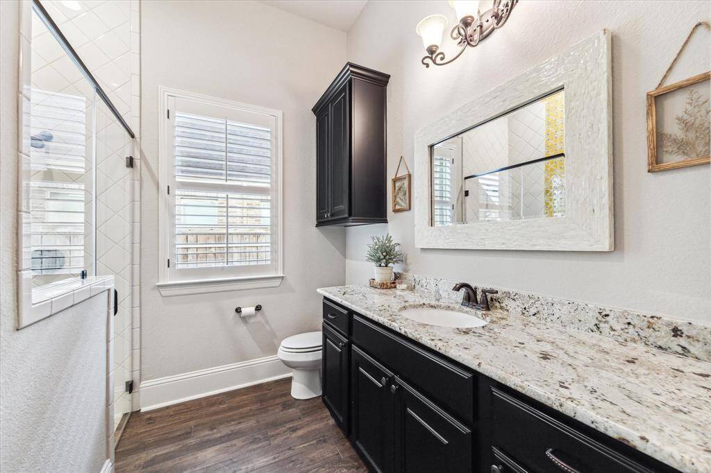 This full ensuite bathroom features a granite-topped extended vanity with a framed mirror, stylish vanity lighting, extra storage, and a fully tiled walk-in shower offering both function and comfort for overnight guests.