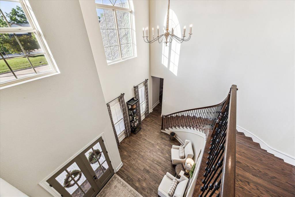 From the second-floor landing, the sweeping staircase and grand two-story foyer make a breathtaking first impression. Oversized arched windows fill the space with natural light, highlighting the elegant chandelier, wood-look tile flooring, and seamless flow into the heart of the home.