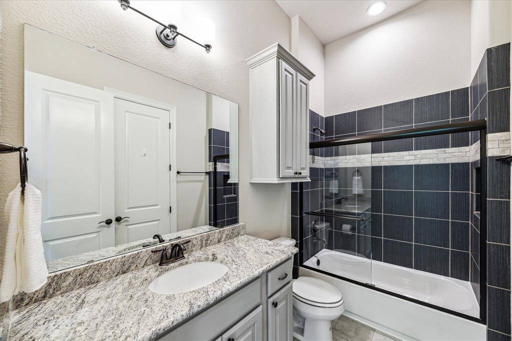 This well-appointed upstairs bathroom features a granite-topped single sink vanity, stylish lighting, and extra storage. A fully tiled tub/shower enclosure completes the space, offering both function and comfort for guests or family.