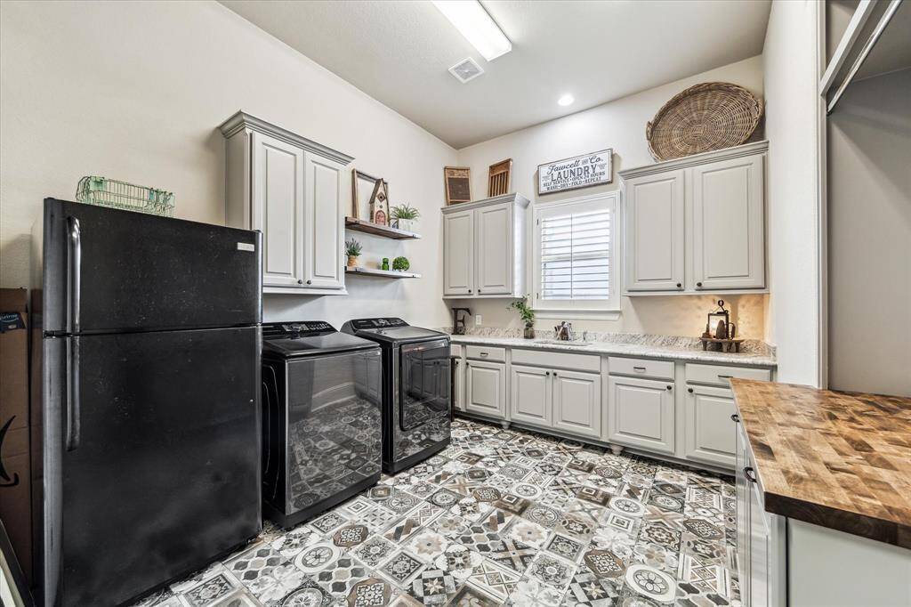 This spacious utility room is as stylish as it is practical, featuring eye-catching custom tile flooring, abundant custom cabinetry, and a combination of granite and butcher block countertops. Outfitted with washer connections, both gas and electric dryer hookups, and a dedicated plug for a second fridge or freezer, it offers exceptional flexibility. Conveniently located near the kitchen, this versatile space also serves as extra storage and prep area, functioning beautifully like a true butler's kitchen.