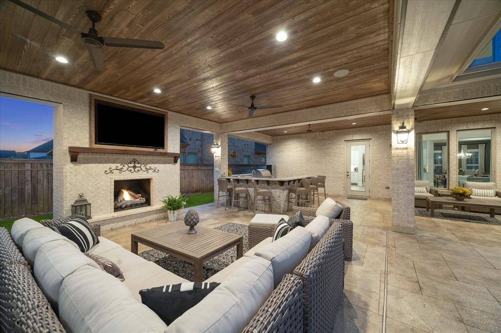 Enjoy exceptional poolside living with the perfect blend of comfort, style, and privacy. Centered around a warm gas-log fireplace, the space features inviting lounge seating beneath a richly stained wood-paneled ceiling with recessed lighting, ceiling fans, and built-in speakers. With no back neighbors and a serene wooded backdrop, it’s an ideal setting for everything from relaxed evenings by the fire to effortless outdoor entertaining.