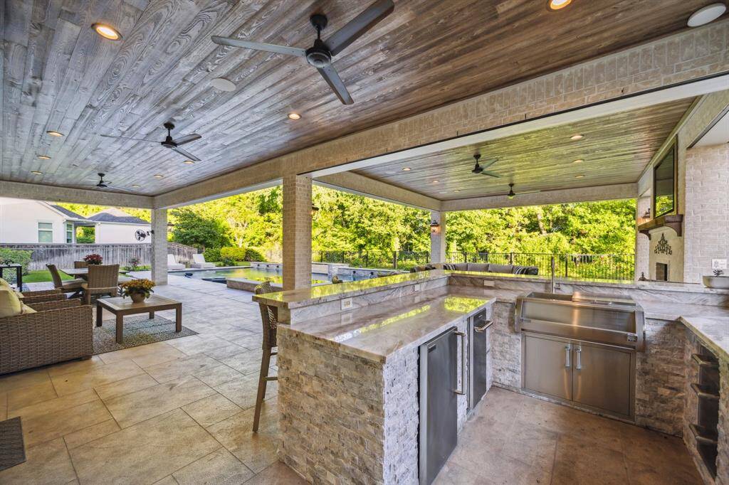 This spectacular outdoor space features a summer kitchen filled with stainless steel Fire Magic appliances. Find a grill, ice maker, beverage butler station sink with cooler, and storage. You'll also enjoy the convenience of built in outdoor speakers, recessed lighting, ceiling fans, and a breathtaking view over your backyard oasis, and into the wooded backdrop. Ask for more info on the amazing indoor/outdoor speaker system!