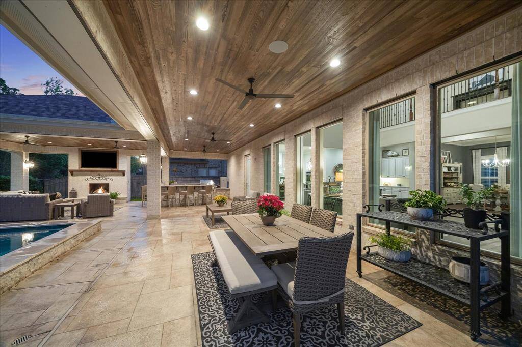 Designed for effortless outdoor living, this expansive poolside covered patio features a fully equipped summer kitchen with Fire Magic stainless steel components, bar seating, a beautiful wood slat ceiling, and speakers. Enjoy open-air dining or unwind in the lounge area, where a gas-log fireplace sets the perfect tone for relaxing evenings. With no back neighbors and a tranquil wooded backdrop, this private retreat seamlessly blends comfort, style, and serenity in one unforgettable setting.